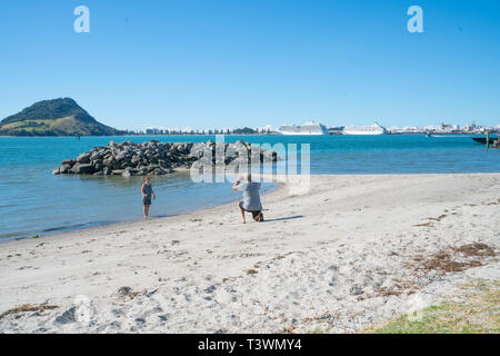 TAURANGA NEUSEELAND - 21. MÄRZ 2019; Paar beim Strand Foto mit Blick über den Hafen von Tauranga Schwefel zu Sehenswürdigkeiten Mount Ma Stockfoto