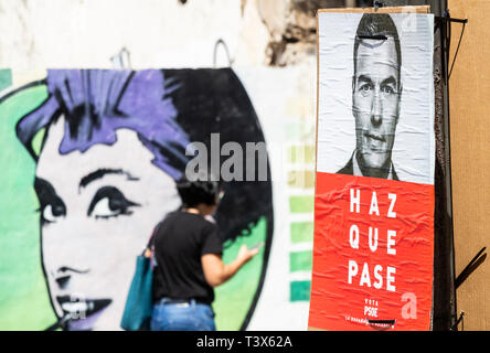 Las Palmas, Gran Canaria, Kanarische Inseln, Spanien. 12. April 2019. Wahlplakate zieren die Straßen von Las Palmas auf den ersten Tag vor den allgemeinen Wahlen in Spanien am 28. April 2019 Werbetätigkeit. Bild: Plakat für die aktuelle Premierminister, Pedro Sanchez der PSOE-Partei. Slogan sagt Haz Que Pase (machen es möglich). Frau vorbei Wandbild von Audrey Hepburn im Hintergrund. Credit: ALAN DAWSON/Alamy leben Nachrichten Stockfoto