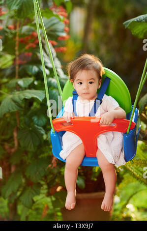 Baby Mädchen auf Schaukeln auf verschwommen grünen Garten Hintergrund Stockfoto