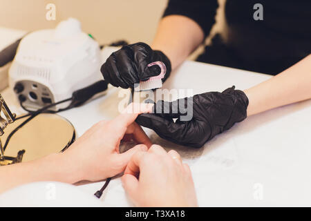 Hardware Maniküre mit elektrischen Gerät Maschine. Verfahren für die Vorbereitung der Nägel vor dem Auftragen von Nagellack. Hände Maniküre in Schwarz Stockfoto