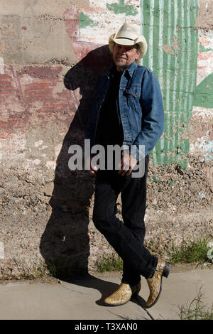 Alte Cowboy, Cowboy Stiefel und einen Hut lehnt sich gegen eine Wand in einer kleinen südwestlichen Stadt in Arizona. Stockfoto