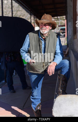 Alte cowboy trägt Cowboystiefel, braun mit genähten Design auf der Seite, blaue Jeans und einem staubigen Leder Cowboy Hut sind. Stockfoto