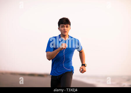 Junge Mann laufen am Strand bei Sonnenuntergang Stockfoto