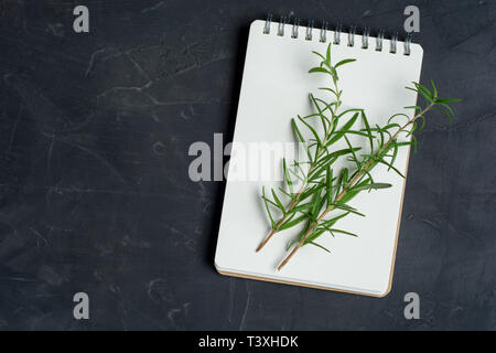 Leere notepad für Rezepte und Zweige frischer Rosmarin auf dunklen konkreten Hintergrund. Kulinarische Konzept. Kopieren Sie Text. Flach. Stockfoto