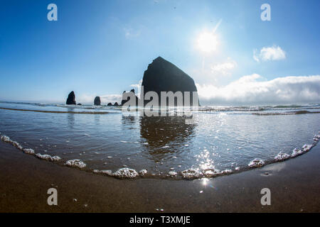 Niedrigen Winkel Ansicht Haystack Rock zu reflektieren, in Wellen des Ozeans, Cannon Beach, Oregon, Vereinigte Staaten von Amerika Stockfoto