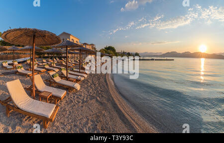 Sonnenliegen und Sonnenschirm am Strand bei Sonnenuntergang auf der Insel Korfu, Griechenland Stockfoto