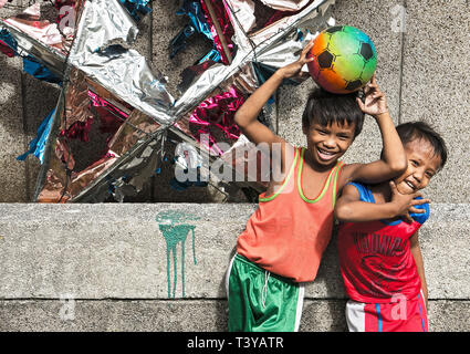 Manila, Philippinen: Zwei Jungen mit einem Fußball lachen und vor einer Wand und eine gebrochene Weihnachten Dekoration posing Stockfoto