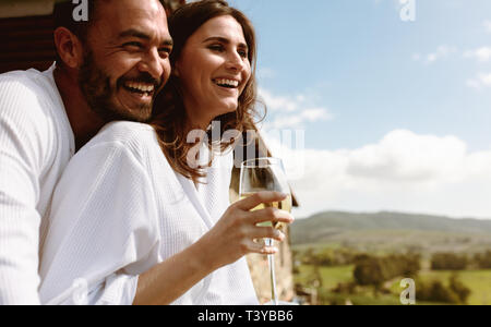 Nahaufnahme von einem lächelnden Paar im Urlaub gemeinsam auf dem Balkon von einem Haus auf dem Land. Lächelnde Frau mit einem Glas Weißwein wi Stockfoto