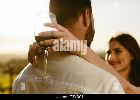 Nahaufnahme von einer Frau mit einem Glas Rotwein mit ihre Arme um ihren Freund stand im Freien. Ansicht von hinten von einem Mann, der mit seiner Freundin Stockfoto