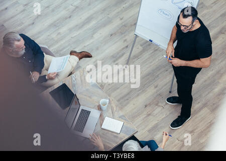 Reifen Geschäftsmann seine Ideen präsentieren auf dem Whiteboard zu Kollegen. Manager eine Präsentation halten, um seine Mannschaft im Konferenzraum im Büro. Stockfoto