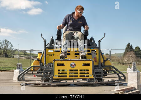 Presteigne, Powys, Wales, UK. Ein Mann mit Aufsitzendem power Trowel (Power float) die Oberfläche eines frisch gelegte Betonplatte Stock zu glätten Stockfoto