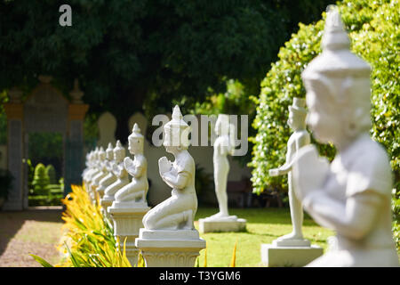 Beten Buddha Statuen aufgereiht in einem Garten am Königspalast in Phnom Penh, Kambodscha, mit einem Tor im Hintergrund. Stockfoto