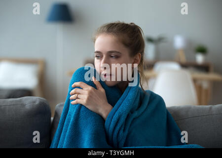Verärgert kranke Frau mit warmen blauen Decke bedeckt, sitzt auf einem Sofa Stockfoto