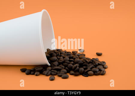 Take-out Kaffeetasse mit dem verschütteten Kaffee Bohnen, orange hinterlegt. Geröstete Kaffeebohnen. Stockfoto