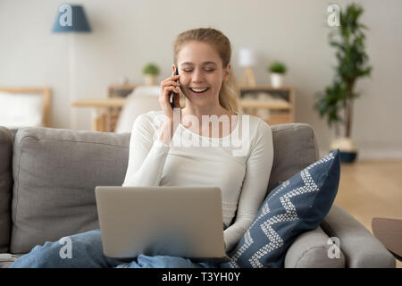Lachende Frau am Telefon sprechen, sitzen auf der Couch, mit Laptop Stockfoto