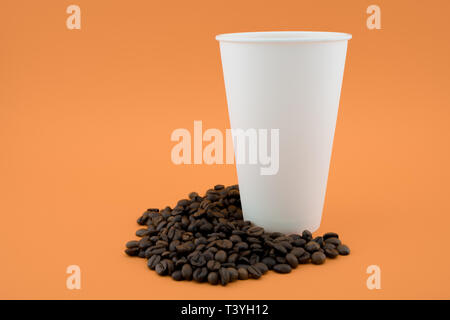 Take-out Tasse Kaffee auf Kaffeebohnen, orange hinterlegt. Die Tasse ist offen, ohne Deckel. Stockfoto