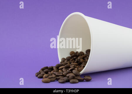 Take-out Kaffeetasse mit dem verschütteten Kaffee Bohnen, violetten Hintergrund. Geröstete Kaffeebohnen. Stockfoto