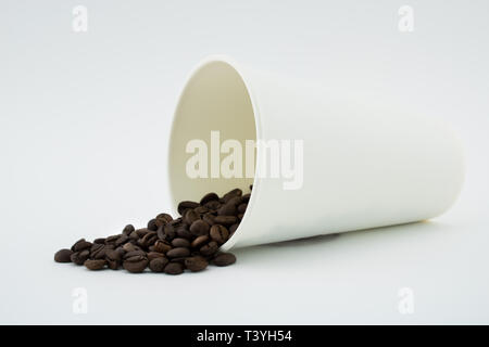 Take-out Kaffeetasse mit dem verschütteten Kaffee Bohnen, weißen Hintergrund. Geröstete Kaffeebohnen. Stockfoto