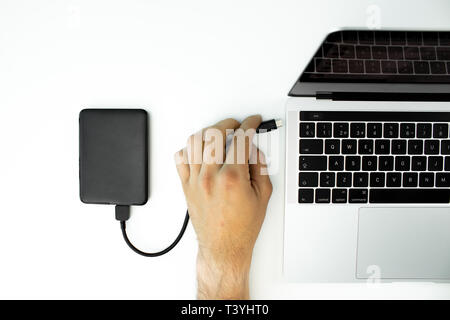 Geschäftsmann eine externe Festplatte an seinen Laptop auf einem weißen Tisch verbunden. Modernen Arbeitsplatz. Stockfoto