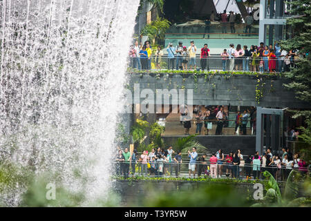 Überfüllte Szene, in der Besucher das Wasser beobachten, das vom oculus am Rain Vortex, Jewel Changi Airport, Singapur, abfließt Stockfoto