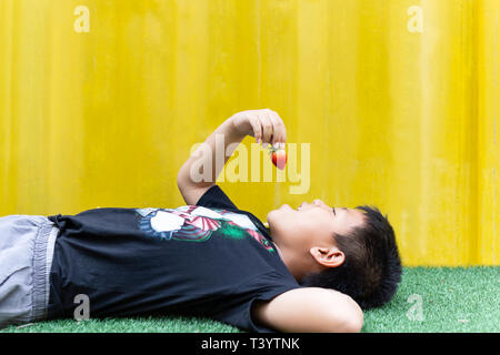 Kleiner Junge liegend Essen Erdbeere im gelben Hintergrund isoliert. Stockfoto