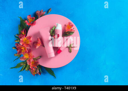 Sonnenschutz und Hautpflege Kosmetik in die rosa Palette in auf einem blauen Hintergrund mit Feder alstroemeria Blumen. Rosa Kreis flach Stockfoto