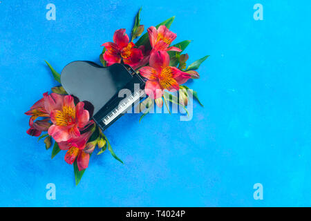 Kleine Piano mit Feder alstroemeria Blumen auf einem blauen Hintergrund mit kopieren. Frühling oder Sommer musikalische Festival Konzept mit Kopie Raum Stockfoto