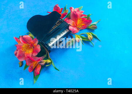 Kleine Piano mit Feder alstroemeria Blumen auf einem blauen Hintergrund mit kopieren. Frühling oder Sommer musikalische Festival Konzept mit Kopie Raum Stockfoto