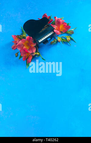 Kleine Piano mit Feder alstroemeria Blumen auf einem blauen Hintergrund mit kopieren. Frühling oder Sommer musikalische Festival Konzept mit Kopie Raum Stockfoto