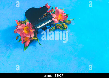 Kleine Piano mit Feder alstroemeria Blumen auf einem blauen Hintergrund mit kopieren. Frühling oder Sommer musikalische Festival Konzept mit Kopie Raum Stockfoto