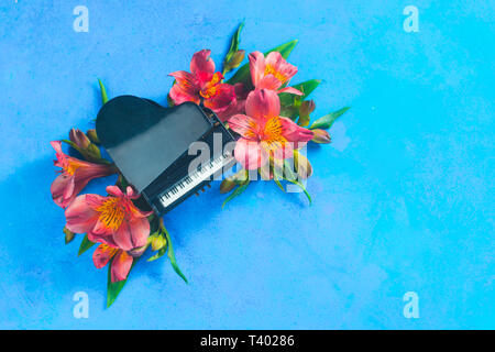 Kleine Piano mit Feder alstroemeria Blumen auf einem blauen Hintergrund mit kopieren. Frühling oder Sommer musikalische Festival Konzept mit Kopie Raum Stockfoto