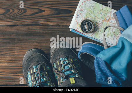 Mehrere Dinge wie eine Karte, einen Kompass, Stiefel und einen Rucksack für eine Wanderung auf einem hölzernen Hintergrund Stockfoto