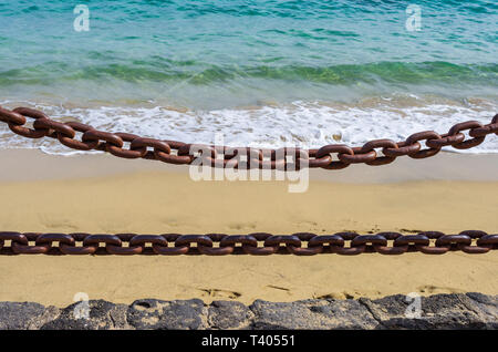 Dicke rostige Ketten mit den Strand, den Sand und das Meer im Hintergrund Stockfoto