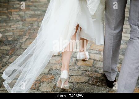 Braut und Bräutigam wandern, Details Braut auf Beinen und weisse Hochzeit Schuhe Stockfoto