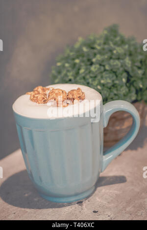 Karamell Popcorn Latte (ohne Koffein) in Hellblau Tasse und Topfpflanze Stockfoto