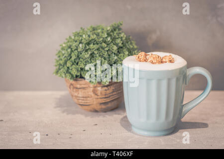 Karamell Popcorn Latte (ohne Koffein) in Hellblau Tasse und Topfpflanze Stockfoto