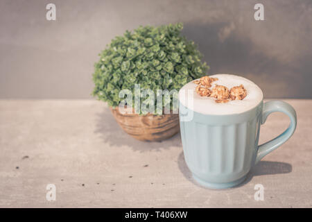 Karamell Popcorn Latte (ohne Koffein) in Hellblau Tasse und Topfpflanze Stockfoto