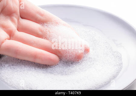Hand mit Schaumstoff von Spülmittel auf dem Hintergrund der Gericht Stockfoto