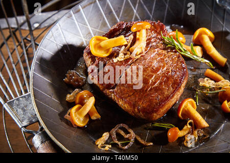 Wild Wild Wild Steak mit Waldpilzen, Zweig Rosmarin und Zwiebeln in eine Pfanne mit Vintage Spachtel serviert. Stockfoto