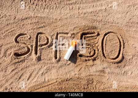 Sun Schutz Faktor 50. SPF 50 Wort auf dem Sand und weiße Flasche mit Sonnencreme geschrieben. Hautpflege Hintergrund. Stockfoto