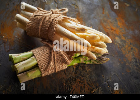 Nahaufnahme auf Trauben von frischen weißen und grünen Spargel gebunden mit rustikalen Hessischen ein String auf rostiges Metall Stockfoto