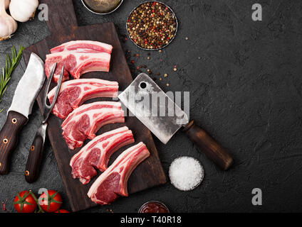 Frische rohe Metzger Lamm rind Schnitzel auf Stein mit Vintage Fleisch Gabel und Messer und Beil auf schwarzem Hintergrund. Salz, Pfeffer und Öl mit tomatoe Stockfoto