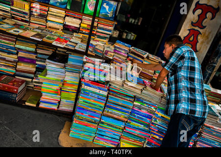 Eine salvadorianische Buchhändler ordnet die Stapel der Bücher auf der Straße in einen gebrauchten Buchhandlung in San Salvador, El Salvador gestapelt. Stockfoto