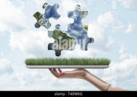 Weibliche hand mit einem Gras und Erde Globus puzzle Stücke oben auf blauem Himmel Hintergrund Stockfoto