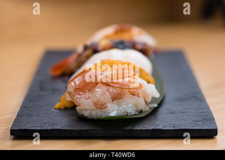 Detail der gedämpfte Garnelen nigiri, mit Hintergrund der Nigiri mit Pacific Seeigel, gedünsteter Lachs, gedämpfte Garnelen, Kaviar, gebratener Aal und Squid, Holz Stockfoto