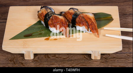 Nigiri gebratener Aal, den Reis Kugel mit einer Algen gebunden, in der Nähe, auf einer Holzplatte mit Stäbchen Stockfoto