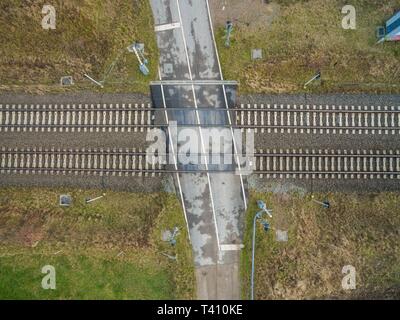 Luftaufnahme von Bahnübergang auf Eisenbahnschienen im Hinterland mit Gras und Bäumen - Blick von oben auf den Gleisen Stockfoto
