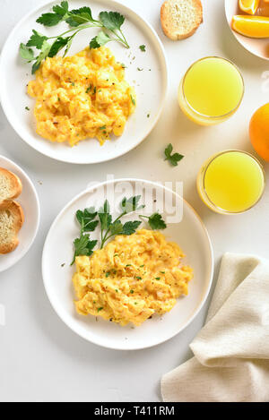 Morgen essen. Rührei auf Platte und Orangensaft über weißen Stein Hintergrund. Ansicht von oben, flach Stockfoto