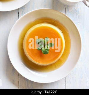 Nahaufnahme von Karamell Pudding Pudding in Schüssel über Holz- Hintergrund. Ansicht von oben, flach Stockfoto