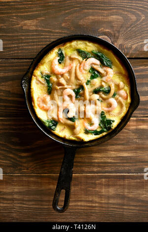 Pilze und Spinat frittata mit Garnelen in einer Pfanne auf Holz- Hintergrund. Ansicht von oben, flach Stockfoto